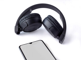 Black wireless headphone and mobile smartphone with a blank screen mockup lay on the surface of a white background
