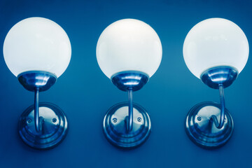 Round wall lights. Three bright lamps against a blue wall. Close-up