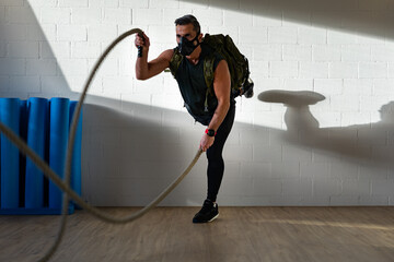 Battle ropes workout with extended leg and training mask. Indoor on oak floor with sun and shadow....