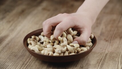 Woman Picks Up A handful Cashew, To Eat, From Her Bowl. took a nut on the right side