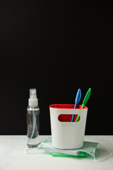 A glass with ballpoint pens, a sanitizer, a medical mask on a black blackboard background. the concept is back to school, in a new reality.
