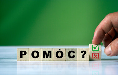 hand turns the wooden cube and changes the polish word POMÓC (english HELP)