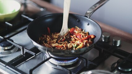 Cook frying noodles and vegetables in wok pan