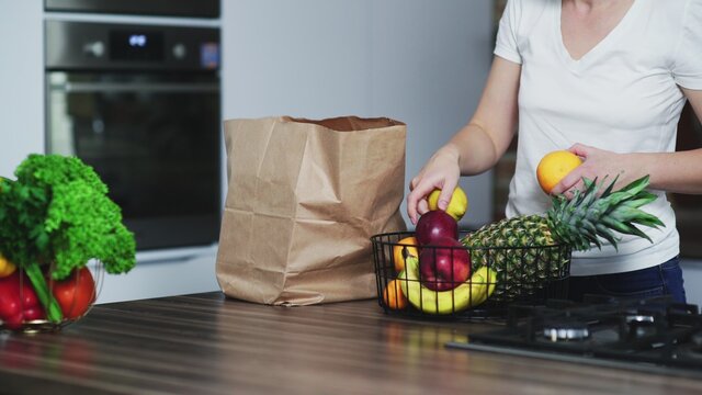 Happy young woman brings to the kitchen a shopping bag with fruits and unpacks it.