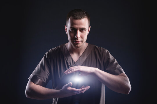 A courageous male masseur makes a passage with his hands, lighting spheres of blue fire between the palms, as the energy of healing and the power of energy practices.