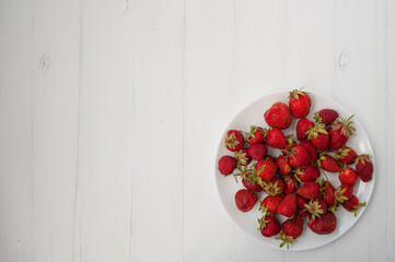 Strawberries on a white plate top view, red berries on a white wooden background, copy space.