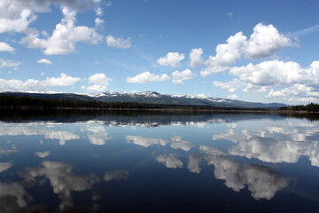 Dynamic cloudy blue skies over mountains, grassy fields, and calm water