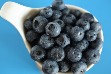 Fresh blueberries in a bowl macro close up on blue background