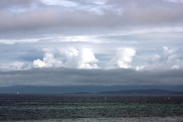 Dynamic cloudy blue skies over mountains, grassy fields, and calm water