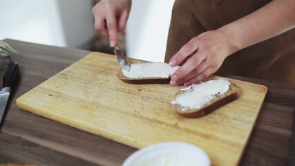 Woman spreading cheese on rye dry toast with a knife.
