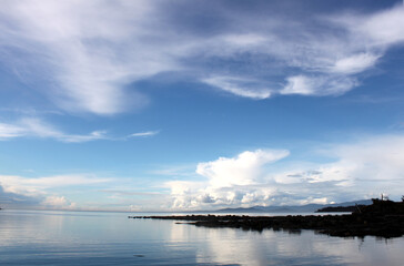 Dynamic cloudy blue skies over mountains, grassy fields, and calm water