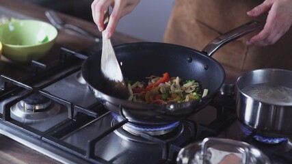 Woman frying vegetables in wok pan at home
