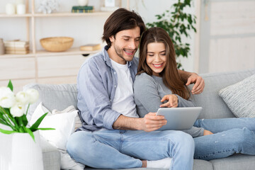 Positive young couple using digital tablet at home