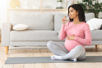 Young black pregnant woman drinking water after training