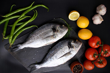two pieces fresh raw atlantic sea fish with vegetables lie on a black stone board, the concept of cooking seefood