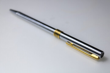 metal pen, with golden and silver colors, in a transversal position, on a white surface