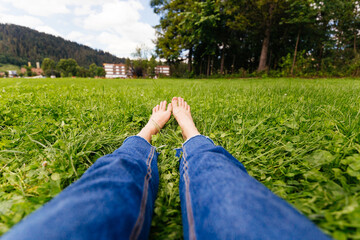 Legs woman relaxing on grass. Female feet on green grass background. Beautiful barefoot legs in the morning dew on the grass.