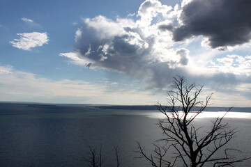 Dynamic cloudy blue skies over mountains, grassy fields, and calm water