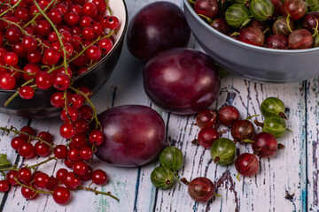 close-up ripe red currant and red-green gooseberry berries in baskets with plums on the table 
