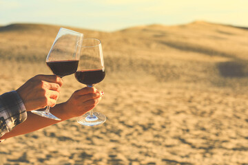 Hands holding red wine glasses on Dune of Pyla during sunset, celebration concept