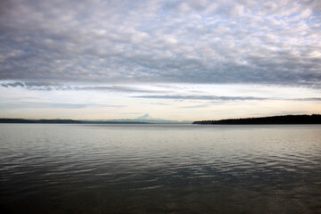 Seascape and shoreline with dynamic cloudy blue skies with reflections in calm water