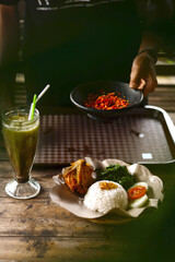 A person who is serving food on the table. Delicious fried chicken rice dish with spicy chili sauce and vegetables. Indonesian special food