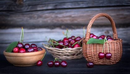 Fototapeta na wymiar wicker baskets and a clay Cup full of ripe cherries against a wooden wall with a copy of the space