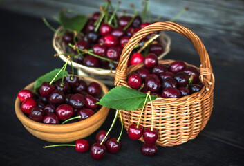 wicker baskets and a clay Cup full of ripe cherries against a wooden wall top view