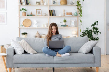 Obraz premium Cheerful young woman using laptop at living room