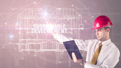 Handsome architect with helmet drawing SUSTAINABLE DEVELOPMENT inscription, new technology concept