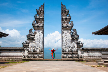A solo tourist taking photos in Hindu temple heaven's gate wearing colourful Sarong with blue...
