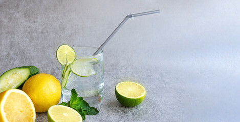 Refreshing lemonade in a clear glass with a straw, with lemon, lime, mint and fresh cucumber, on a gray background. Banner, selective focus, close-up, copy space