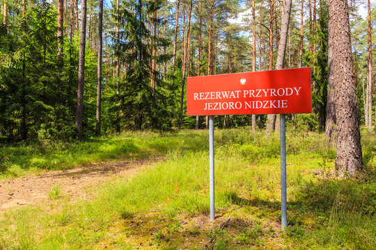 Red sign "Rezerwart Przyrody Jezioro Nidzkie" which translation is "Nature Reserve Lake Nidzkie" near forest cycling path in Puszcza Piska, Mazury Lake District, Poland