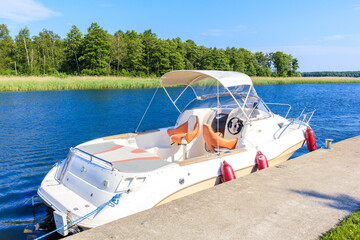 Fototapeta premium Luxury motorboat anchoring in Pisz sailing port on Lake Ros on summer sunny day, Masurian Lakes, Poland