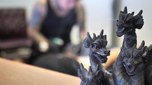 Smoke blowing out of multiple dragon head statue figures as Caucasian white tattoo artist with black latex gloves tattoos client in background. Shot in 4K 60fps, slowed to 30fps.