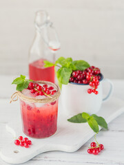 Summer drink with white sparkling wine. Homemade refreshing fruit cocktail or punch with champagne, red currant, ice cubes and mint leaves on white wooden background