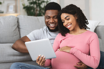 Fototapeta premium Pregnant couple having fun at home, using digital tablet together