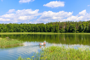 MOKRE LAKE, POLAND - JUN28, 2020: Couple of people sailing with small fishing boat on Krutynia river to Mokre lake, Masurian Lakes, Poland.