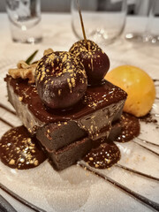 Rich chocolate brownie with orange ice cream and melted chocolate on top with golden decoration