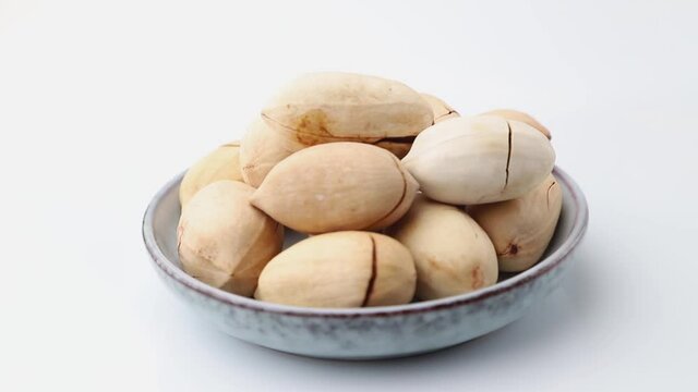 Rotating of raw pecan nuts in ceramic plate on white background. Side view, close up.