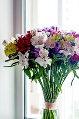 Alstroemeria bouquet of flowers in a vase by the window. Beautiful bouquet of colorful flowers in the apartment by the window.