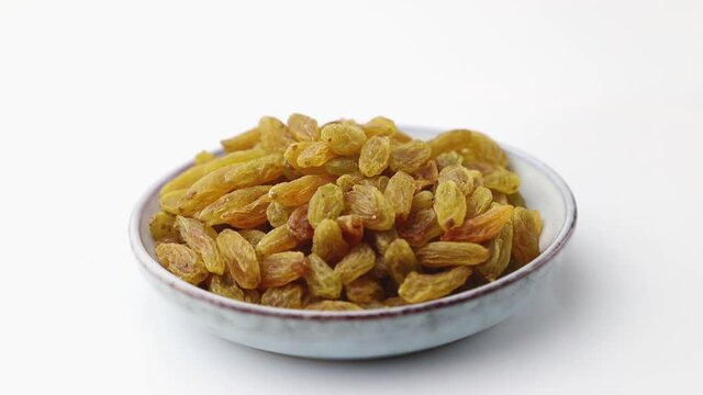 Rotating of raisins in ceramic plate on white background. Side view, close up.
