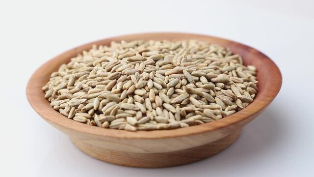 Rotating of rye grains in wooden plate on white background. Side view, close up.