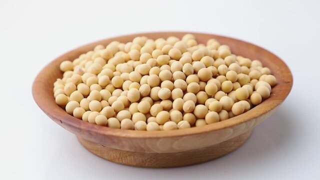 Rotating of soy seeds in wooden plate on white background. Side view, close up.