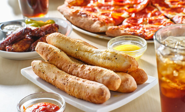 garlic butter breadsticks with soda and pizza in background