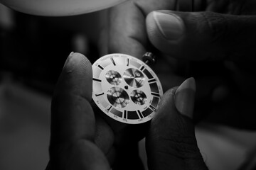 Watchmaker examining the dial and crown of a watch. Black and white photo.