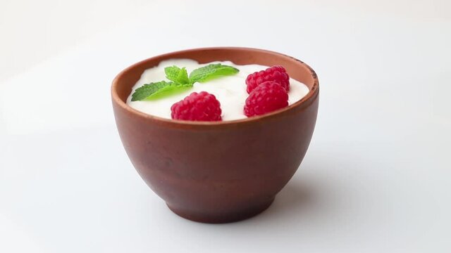 Rotating of yogurt with raspberry in clay cups on white wooden background. Side view, close up.