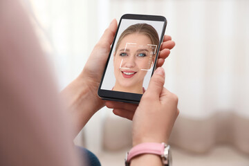 Woman using smartphone with facial recognition system indoors, closeup. Biometric verification