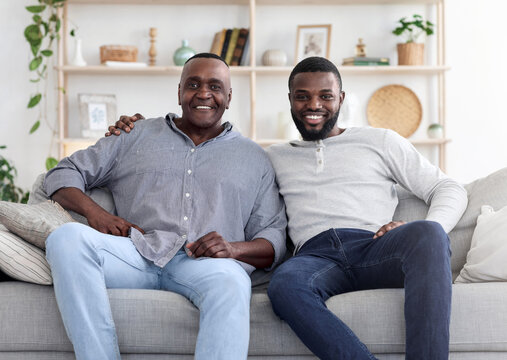 Adult black son and his senior father posing on couch at home