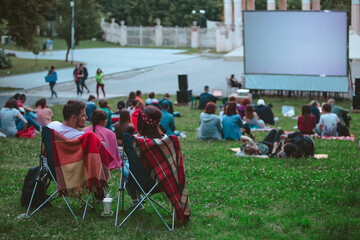 couple sitting in camp chairs in front of movie screen at open air cinema